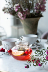 hot fruit tea with cranberries and apples in a glass teapot on a light background. selective focus.