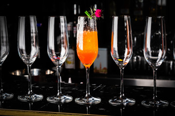 Composition with tall glass cocktail glass with orange cold drink, ice cubes melting on a dark shiny surface on a deep black background
