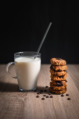 Oat chocolate cookies stacked next to a cup of milk over a wooden table