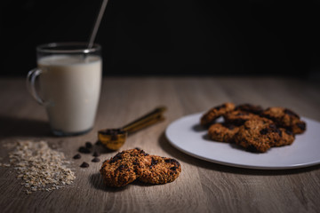 Oat cookies over a wooden table with a cup of milk and chocolate chips