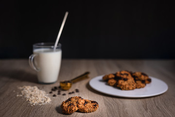 Oat cookies over a wooden table with a cup of milk and chocolate chips