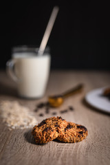 Oat chocolate cookies close up with a cup of milk, rolled oats and chocolate cookies