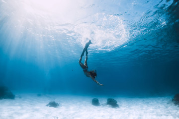 Woman free diver with fins glides over sandy bottom near corals underwater in blue sea