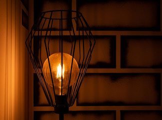 Klimatyczna lampa w starym oldschool stylu na tle malowanych cegieł muru, oświetlająca ciepłą...