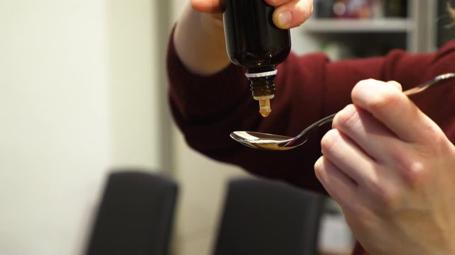 female hands pouring medicine drops onto tablespoon at home