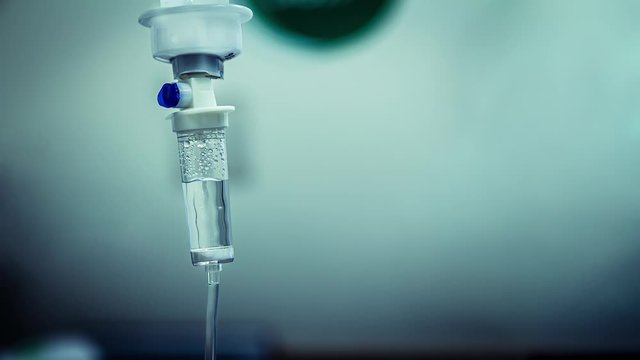 Cinemagraph of a fluid intravenous saline drip in a hospital room. Close up on Set IV fluid intravenous drop saline on a dark blue light background. Loop, selective focus, and copy space.
