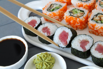 Fresh prepared sushi. Maki with tuna and California close up. Chopsticks taking portion of sushi roll on the table restaurant. Eating Japanese food
