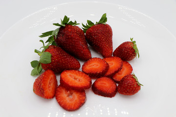 White plate with whole and sliced strawberries