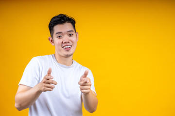 Young handsome Asian man with beard over isolated yellow background points finger at you while smiling