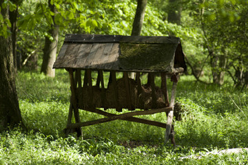 Naklejka premium Cratch with hay and cereal grains for wild animals in forest.