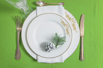 Festive table setting for Christmas dinner. Two white plates, vintage fork and knife on green fabric background. Top view