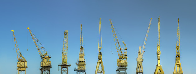 Row of majestic old harbor cranes in Antwerp with early morning sky.