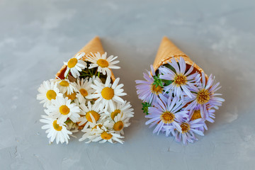 Obraz premium Bouquet of chamomiles in a waffle cone on a gray background. The flowers are blooming. Wildflowers.