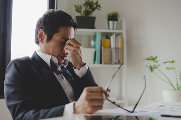 tired asian young businessman feeling stressed and taking off eyeglasses feels eye strain fatigue...