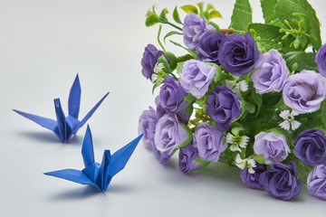 Blue origami crane and purple flowers, shallow depth of field