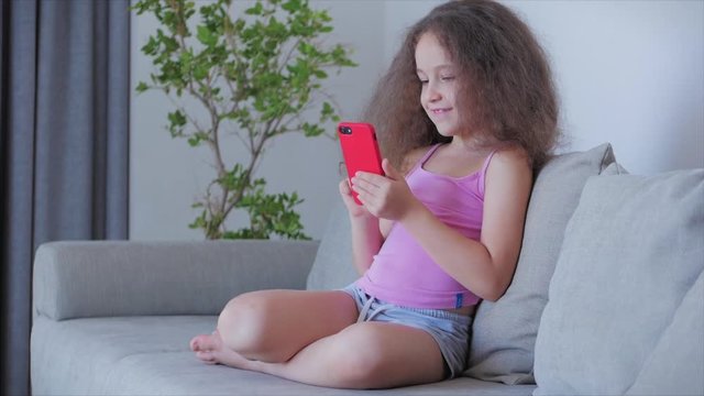 Curious cute boy preschool child using a digital tablet technology device looks telephone.Plays in the phone sitting on the sofa alone.Children tech addiction concept play game at home.