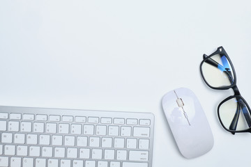 Workplace with keyboard, mouse and glasses on a white table with copy space and top view.