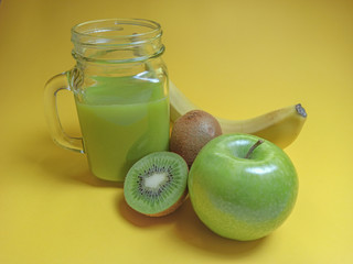 Green healthy smoothie in glass jar: banana, kiwi, green apple. Healthy drink on yellow background.