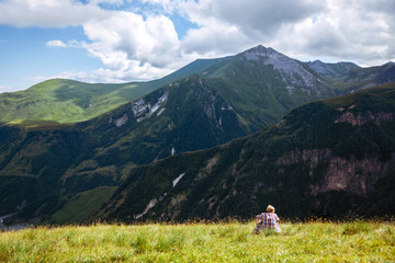Traveler hiking alone young man sits on a green meadow in front of a mountain landscape. Summer time. Travel. Georgia. adventure, active, lifestyle, vacations, outdoor - 347544959
