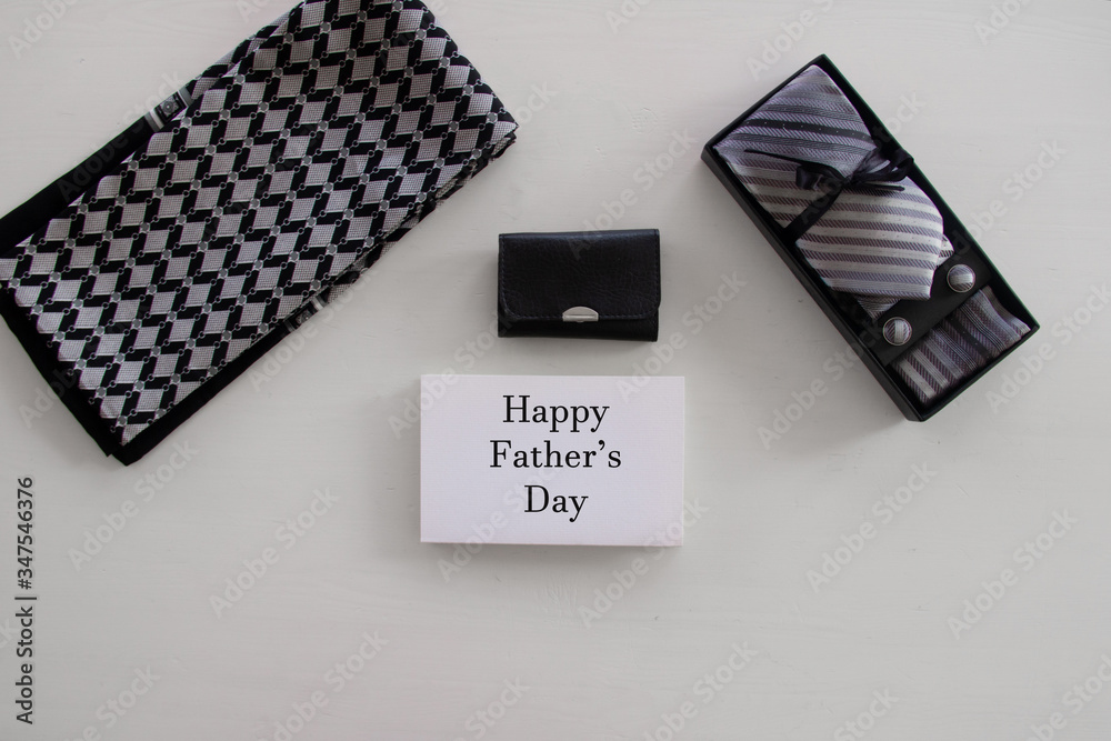 Wall mural Happy Fathers Day inscription with tie, tool kit or wallet, mens scarf, box with a tie and cufflinks with a bow on white background. Greetings and presents. white card, congratulationfor man, flatlay