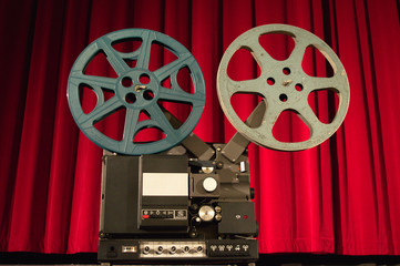 Old movie projector in the cinema with red velvet curtain in the background © Agata