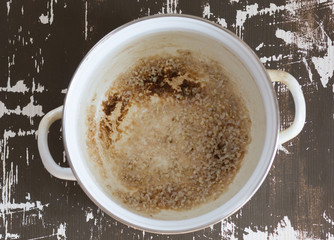Top view of pan with burnt bottom after cooking porridge on the brown background.