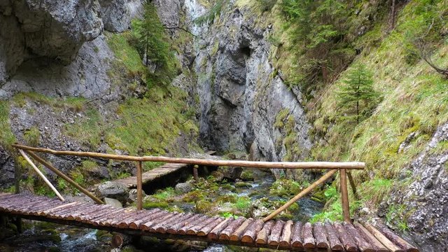 Slow flight through a narrow passage of a canyon above a footbridge and a stream