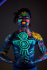 portrait of strong muscular male covered with fluorescent luminescence body art glowing on neon light