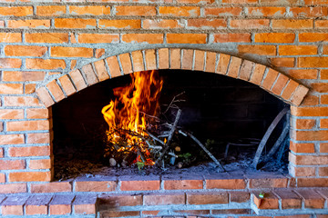 Branches are burning inside fireplace made of bricks