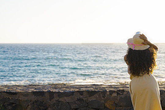 Woman looking at the sea during the summer day on the beach. Young woman wearing a hat in sunlight looking far away. Free space to write down - Image