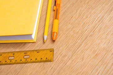 Yellow notebook, yellow pen, yellow pencil and yellow ruler on a wooden table surface. Stationery of the same color. Office supplies. Free space for text. Bright business concept.