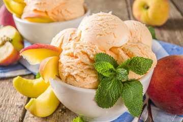 Homemade sweet peach ice cream. Peach gelato balls in small bowls, on wooden background with fresh peaches and mint leaves - obrazy, fototapety, plakaty