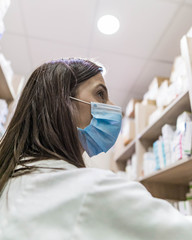 Pharmacist working during a coronavirus pandemic and wearing an anti-virus mask. Pharmacist looking for a medicines.