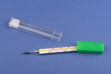 Glass mercury thermometer and case for thermometer on a blue background.