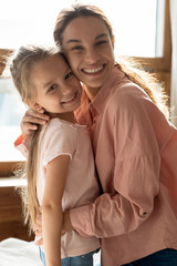 Head shot vertical portrait happy smiling mother and adorable little daughter hugging, looking at...