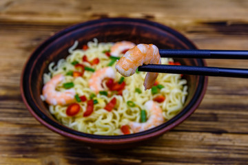 Instant noodle with shrimps, red pepper and green onion in a ceramic bowl. Japanese food. Chopsticks with shrimp