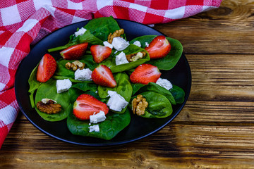 Salad with spinach leaves, feta cheese, walnuts and strawberry on a black plate