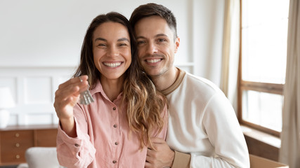 Head shot portrait happy young couple showing keys from first new house, purchasing real estate,...