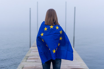 Yyoung girl who loves Europe holding the European Union flag, confident of her beliefs and loving Europe on the pier during a cloudy day. 