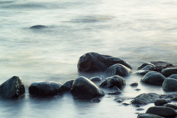 Long exposure of sea and rocks. Boulders sticking out from smooth wavy sea. Tranquil scene