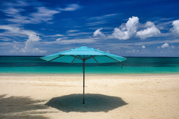 Horizontal image of an empty Cayman Island Beach with an open blue beach umbrella