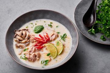 Tom Kha Gai or Thai Coconut Chicken Soup in matte gray bowl on concrete backdrop. Tom Kha Gai is Thailand cuisine dish with coconut milk, chicken, galangal, lemongrass, mushrooms, lime. Thai Food