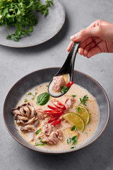 Tom Kha Gai or Thai Coconut Chicken Soup in matte gray bowl on concrete backdrop. Tom Kha Gai is...
