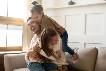 Excited father having fun with two little daughters, spending weekend at home, sitting on...