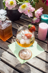 Cocktail on a wooden table in the sun with flowers and candles
