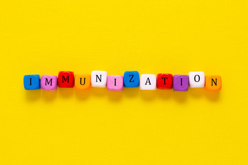 Immunisation word made from colorful cubes over yellow background, top view.