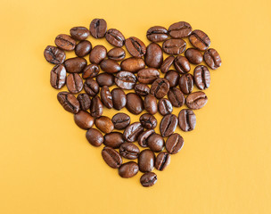 Coffee beans laid out in the shape of a heart on a yellow background. Love coffee.