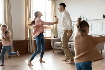 Fototapeta na wymiar Happy family with two daughters dancing, moving to favorite music in living room, spending free time together, cute preschool girls having fun with excited father and mother, celebrating relocation