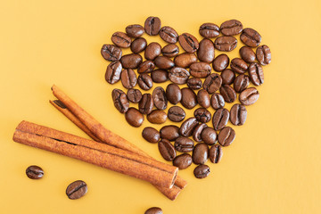 coffee beans and cinnamon sticks. Coffee beans laid out in the shape of a heart with cinnamon sticks on a yellow background. Love for coffee.