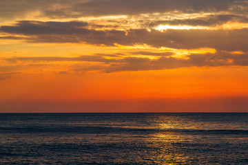 Beautiful sunset on the sea. The rays of the setting sun Shine through the clouds in the orange sunset sky. A luminous path from the sun on the sea surface.